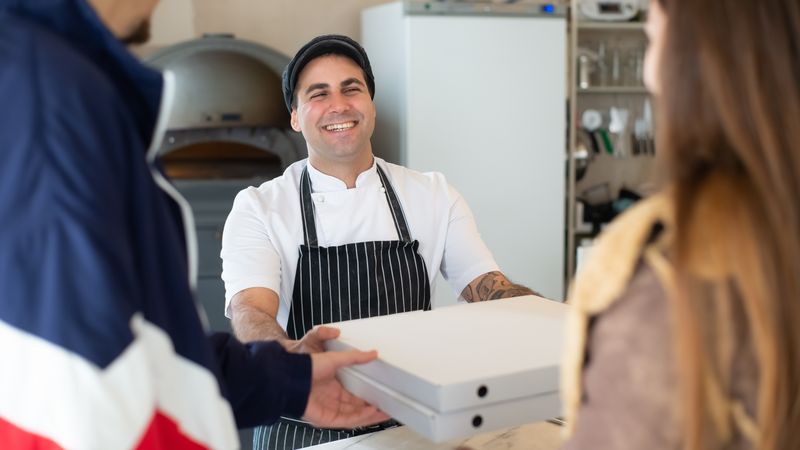 Pizzaiolo entregando caixas de pizza a clientes no balcão da pizzaria